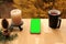 On a wooden table vertically lies a modern telephone with pre-keyed green screen, on the right is a black mug with tea on terrace