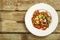 On a wooden table is a white plate of boiled mung bean with vegetables and mushrooms. Copy space.