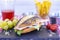 Wooden table with white and red rustic napkin. A poppy seed sandwich stuffed with ham, cheese, tomato and lettuce. French fries