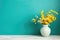 Wooden table with yellow vase with bouquet of field flowers near empty, blank turquoise wall. Home interior background