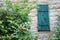 Wooden Teal Green door Window on a rough hewn log cabin side with a bush