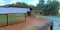 Wooden terrace of a luxurious country house with a swimming pool. Fencing made of glass panels and metal fasteners. Thick bushes