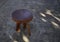 Wooden three legged stool, tripod, on a concrete base