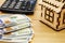 Wooden, toy house, dollars and calculator on a wooden background.