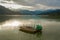 Wooden traditional boat floats on the Pokhara lake in Nepal. Sunlight shines on the water and the mountains are at the back in dif