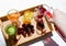 A wooden tray with colorful drinks: orange, yellow, and cucumber lemonade. Nearby are cherries. A hand pours red juice from a