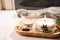 Wooden tray with decorated scented candles on white table