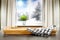 A wooden tray with table cloth on the table. Snowy winter background utside the window and space for products and decorations.