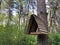 Wooden triangular brown birdhouse on high tree in green forest.
