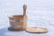 A wooden tub for water stands on a slice of a tree trunk on ice on a blurry snow background.