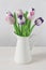Wooden tulips artificial flowers pink violet in a white jug, vertical. Flower still life in bright colors. Bouquet of artificial