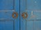 Wooden, vintage, full-blue door with orange doorknobs on each door.