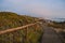 Wooden walkway with hill with fence and carpobrotus edulis cactus, footpath in seascape at SÃ£o Paio beach, cliffs and horizon fog