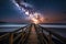 a wooden walkway leading to the ocean under a night sky filled with stars and a milky filled sky above the ocean and a wooden