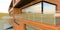 Wooden wall of a suburban house. Mirror reflection windows. Spacious terrace with fence made of glass and steel fittings. 3d