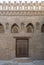 Wooden weathered door, perforated stucco window decorated with floral patterns, and three steps on stone bricks wall