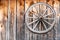 A wooden wheel with a metal hoop hangs on a wall made of old wooden planks.