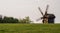 Wooden windmill on the hillside against a background of trees and blue sky.