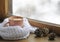 Wooden winter window. A cup of hot coffee and a warm white knitted scarf on the windowsill. Still life