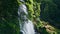 Woodland waterfall falling rocks closeup. Drone shot vivid water cascading mossy
