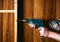 Woodworker drills a hole with an electric drill in wood board. Closeup of foreman hand at work. Working environment in carpentry