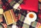 Woolen plaid, cup of tea, old books, red pillow on wooden background. Top view. Toned