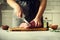 Wooman hands cutting beef meat on wooden chopping board, rosemary, oil, salt, pepper. Girk cooking pork meat on white