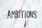 Word `ambitions` handwritten on crumpled torn paper, top view.