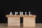 Word April written on wooden blocks. Black background. Spring calendar
