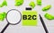 The word B2C BUSINESS TO CONSUMER written on a green sticky note next to a magnifying glass and a black marker on a wooden table