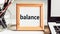 The word balance in a wooden frame on a table with a laptop and pens. Business concept