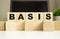 The word BASIS is written on wooden cubes lying on the office table in front of a laptop.