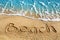 Word BEACH written on yellow sand, blue sea wave, white foam top view close up, handwriting letters text, summer vacation, holiday