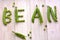 Word `bean` of raw, fresh pots and peas background. Split, green peas on wooden board.