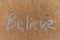 The word Believe written with sidewalk chalk on gray concrete pavement background