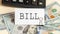 The word BILL is written in a notebook next to the bills and a black calculator. Business concept