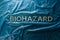 The word biohazard laid with silver letters on blue crumpled plastic film background in flat lay composition at center
