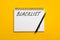 Word Blacklist written in notepad on yellow background, top view