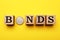 Word Bonds made of wooden cubes with letters and coin on yellow background, flat lay