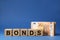 Word Bonds made of wooden cubes with letters and euro banknotes on blue background