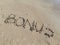 Word `Bonus` written on wet sand at the sea