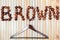 Word brown is lined with ripe large chestnuts and wooden clothes rack in close up on light wood background. Color matching