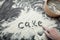 The word `cake` is written on the background of flour from a woman`s hand.