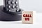 The word call us on wooden block with telephone background. Business concept for customer service or consultancy