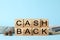 Word Cashback made with wooden cubes, coins and banknotes on light blue background