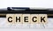 A word Check written in a wooden cube with a pen and wallet
