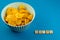 The word chips is lined with wooden letters. A bowl of potato chips on a blue background with copy space. Party snack. Top view