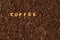 The word COFFEE  made from biscuit letters on a dark coffee bean background