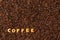 The word COFFEE  made from biscuit letters on a dark coffee bean background