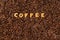 The word COFFEE  made from biscuit letters on a dark coffee bean background